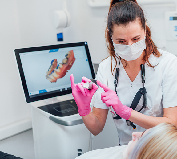 Dentist with mask showing patient a piece of technology