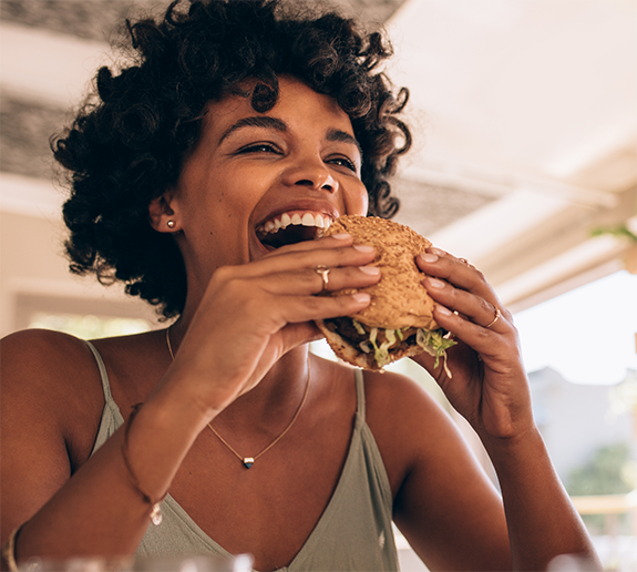 Woman with curly hair taking bite out of a burger