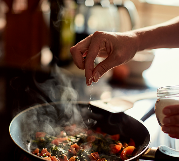 Sprinkling seasoning on food in pan