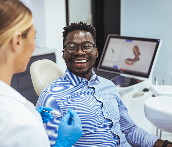Man in button up shirt sitting in dental chair and smiling