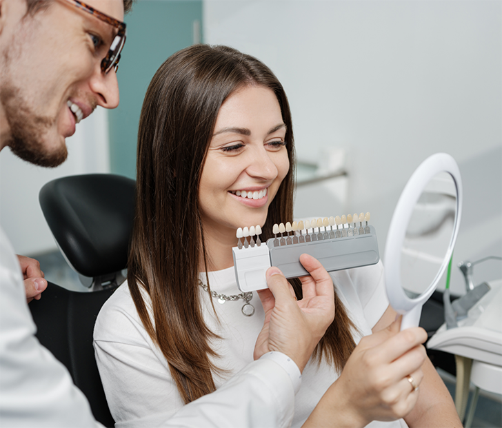 Female patient looking in mirror while dentist holds up shade guide